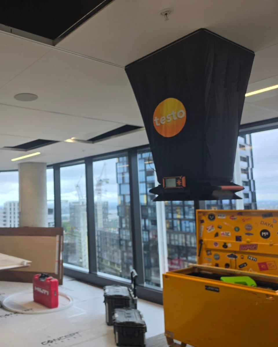 Capture hood mounted overhead on a commercial fit-out while work continues below