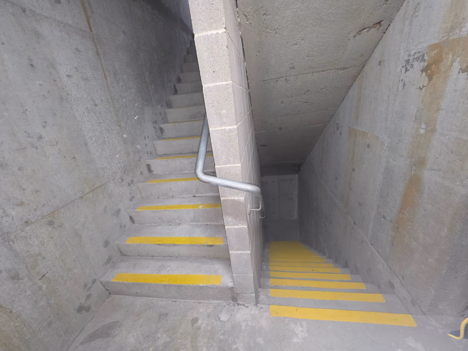 Concrete fire-egress stairwell with yellow step nosings and handrail in a commercial building, tested for stair pressurisation